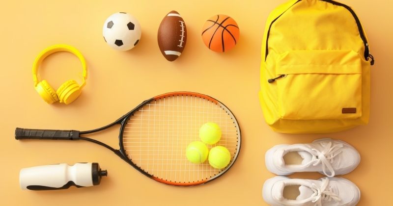 Różne akcesoria sportowe, piłki, rakiety, bidon, słuchawki, żółty plecak, buty sportowe białe, 